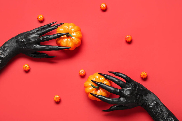 Manos negras de bruja con calabazas sobre fondo rojo. Halloween celebración - Foto, Imagen