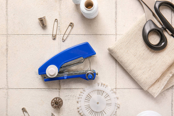 Ручна швейна машина з різними приладдям на фоні білої плитки - Фото, зображення
