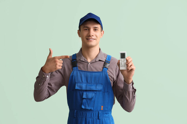 Мужчина-техник с пультом дистанционного управления с кондиционером показывает большой палец вверх на зеленом фоне - Фото, изображение