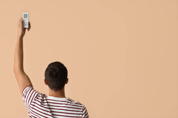 Jongeman met airconditioner afstandsbediening op beige achtergrond, achteraanzicht - Foto, afbeelding