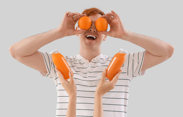Νεαρός με πορτοκάλια και μπουκάλια χυμού σε ελαφρύ φόντο - Φωτογραφία, εικόνα