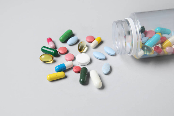 Potje met verschillende verspreide pillen op grijze achtergrond - Foto, afbeelding