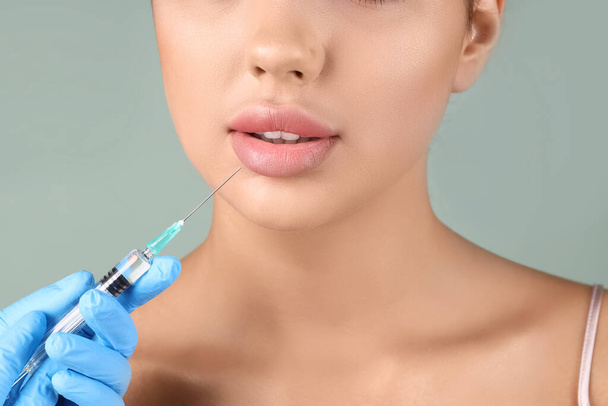 Mujer joven recibiendo inyección de labios sobre fondo verde, primer plano - Foto, imagen