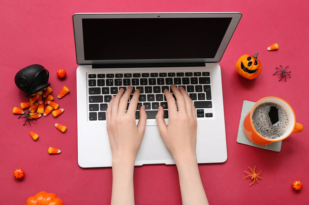 Woman with coffee cup and Halloween candies using laptop on red background - Photo, Image