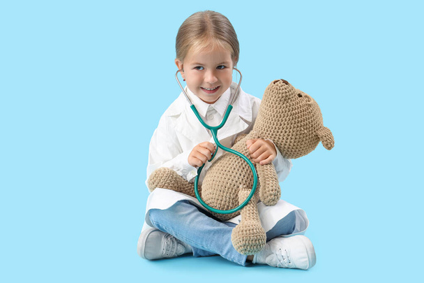 Χαριτωμένο μικρό γιατρό με στηθοσκόπιο και αρκουδάκι σε μπλε φόντο - Φωτογραφία, εικόνα