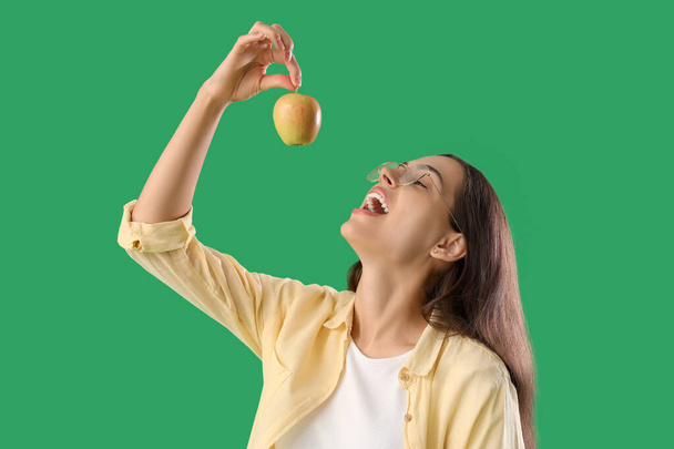 Ładna młoda kobieta je dojrzałe jabłko na zielonym tle - Zdjęcie, obraz