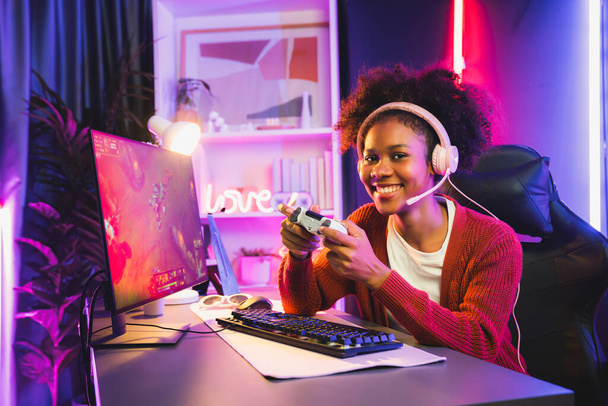 African American girl gaming streamer team winner playing online fighting with Esport wearing headphones in neon lighting room. Talking other players planing strategies to win competitors. Tastemaker. - Photo, Image