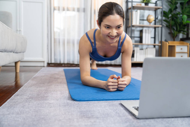 Fit młoda azjatycka kobieta struganie na podłodze w salonie podczas wykonywania instrukcji ćwiczeń na wideo szkolenia online. Zdrowy styl życia ćwiczenia rutynowe w domu. Równowaga i wytrzymałość. Energiczny - Zdjęcie, obraz