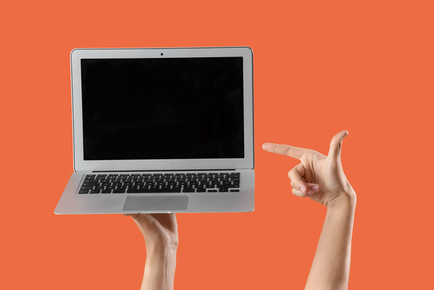 オレンジ色の背景に空白のノートパソコンを指している女性 - 写真・画像