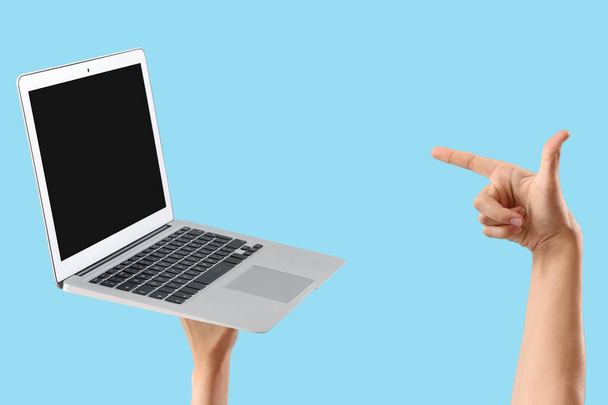 Vrouw wijzend naar lege laptop op blauwe achtergrond - Foto, afbeelding