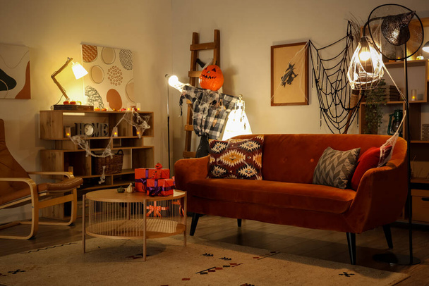 Интерьер праздничной гостиной с украшениями на Хэллоуин, светящимися лампами, коричневым диваном и журнальным столиком - Фото, изображение