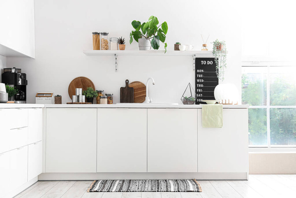 Λευκοί πάγκοι με νεροχύτη, φυτά σπιτιού και σκεύη στο εσωτερικό της σύγχρονης κουζίνας - Φωτογραφία, εικόνα
