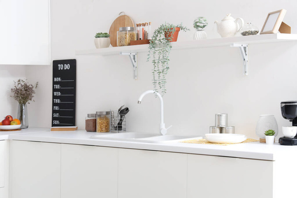 Intérieur de la cuisine lumineuse avec comptoirs blancs, étagère, évier et ustensiles - Photo, image