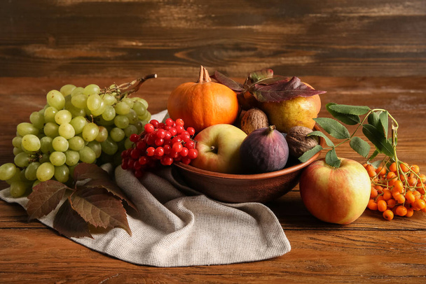 Чаша с различными свежими фруктами, тыквой и ягодами на деревянном фоне - Фото, изображение
