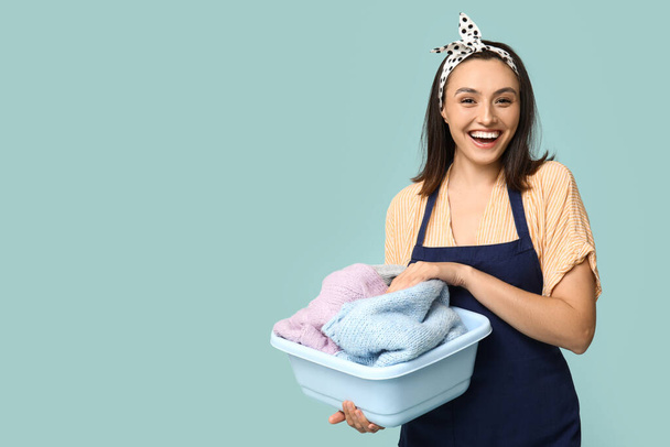 Portrait of happy young housewife in apron with dirty laundry on blue background - Photo, Image