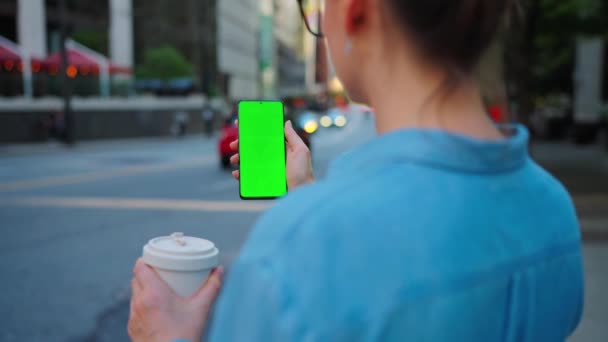 Kobieta stoi na ulicy i za pomocą smartfona z zielonym ekranem, widok z tyłu. Komunikacja, dzień pracy, pracowite życie. Zwolniony ruch - Materiał filmowy, wideo