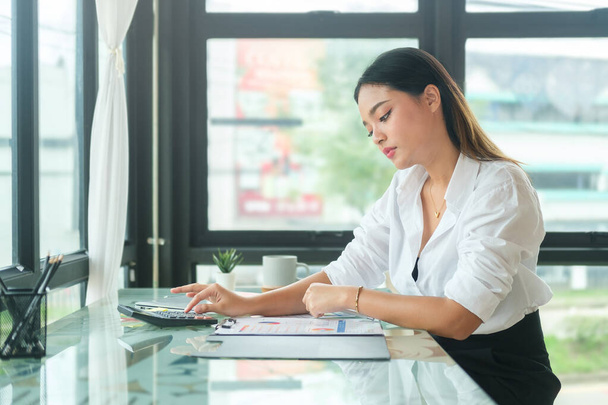 Nachdenkliche asiatische Geschäftsfrau überprüft Finanzberichte am Schreibtisch ihres Büros. - Foto, Bild