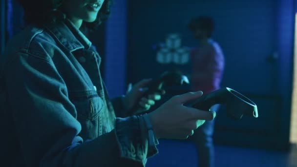 Primer plano de mujer joven con auriculares VR, con controladores de mano jugando juego de disparos en la simulación de realidad aumentada en la arena oscura vacía con luz de neón azul en el ciberclub - Metraje, vídeo