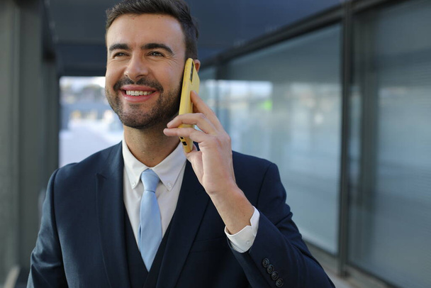 портрет красивого молодого бизнесмена в костюме со смартфоном на городской улице - Фото, изображение