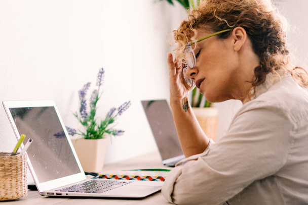Втомлена жінка торкається шиї та окулярів перед ноутбуком на робочому місці домашнього офісу. Малий бізнес комп'ютерні технології сучасні люди концептують спосіб життя. Стрес і проблеми ноутбукового бізнесу - Фото, зображення