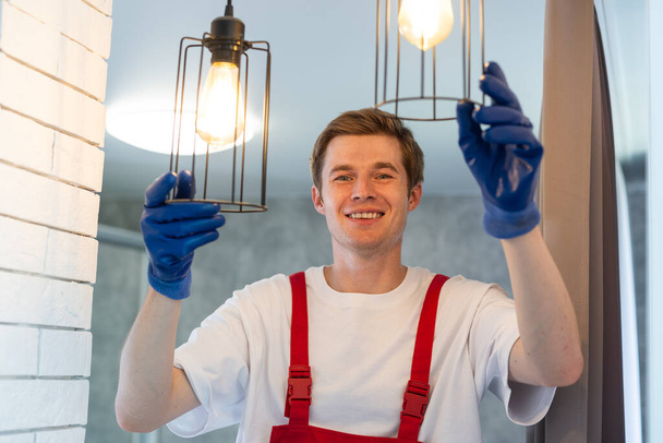 Jeune homme installant une lampe de plafond sur escabeau dans la cuisine. - Photo, image