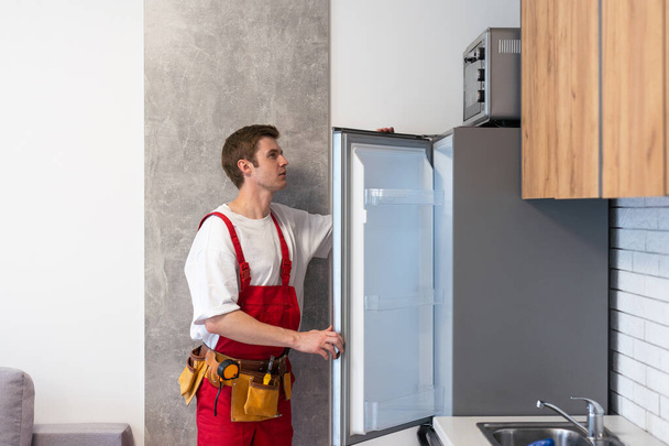Werknemer repareert koelkast in keuken. - Foto, afbeelding