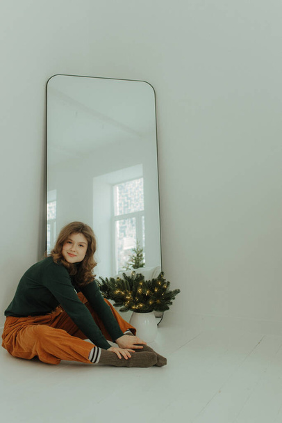 Neşeli gülümseyen genç bir kız Noel tatili için hazırlanıyor ve evin samimi bir iç odasında bir Noel ağacı süslüyor. Seçici odak. - Fotoğraf, Görsel