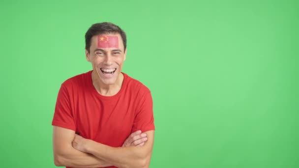 Video in studio with chroma of a Man standing with chinese flag painted on face smiling with arms crossed - Footage, Video