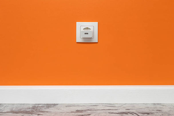Valkoinen pistorasia asennettu oranssi seinä, jossa on asennettu puhelin sovitin, etunäkymä. - Valokuva, kuva