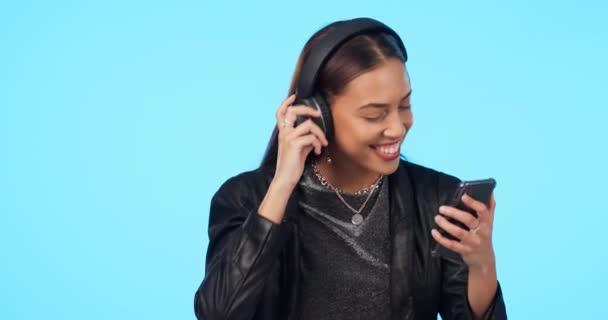 Woman, dancing to music with smartphone and headphones, listening to playlist and energy on blue background. Young female person, audio streaming and radio, happiness and gen z with mockup space. - Footage, Video