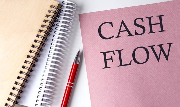 CASH FLOW slovo na růžovém papíru s kancelářskými nástroji na bílém pozadí - Fotografie, Obrázek