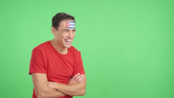 Βίντεο στο στούντιο με chroma ενός ευτυχισμένου ανθρώπου με κουβανέζικη σημαία ζωγραφισμένη στο πρόσωπο κοιτάζοντας μακριά στο χώρο αντίγραφο στο κενό - Πλάνα, βίντεο