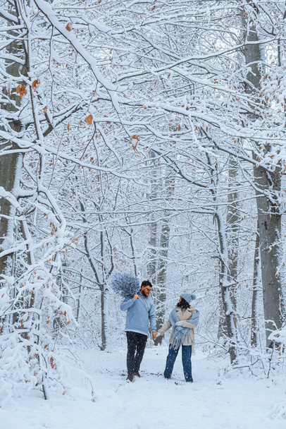 A téli erdőben a pár együtt sétál. karácsonyfa van a vállán. - Fotó, kép