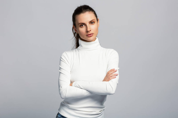 Portrait of a woman looking very confident with arms crossed, on light grey studio background - Photo, Image