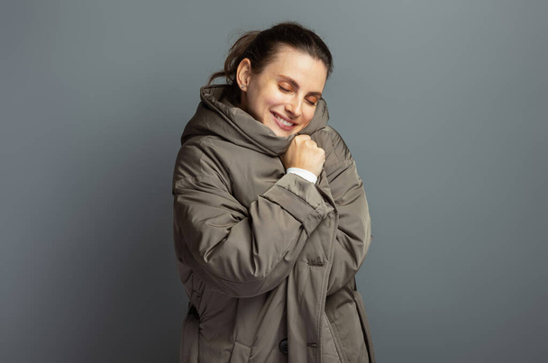 Mladá veselá atraktivní žena v šedém kabátě během podzimu a zimy, izolované na šedém pozadí studia - Fotografie, Obrázek