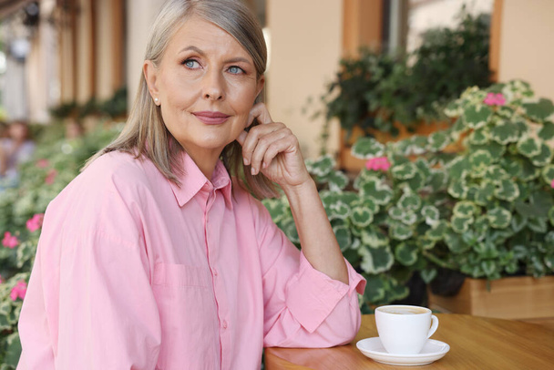 Portrait of beautiful senior woman with cup of coffee at table in outdoor cafe - Foto, imagen