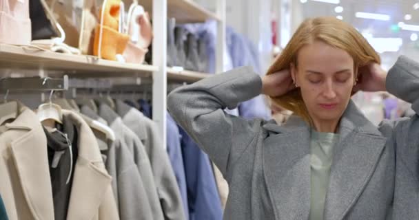 Lady probeert een trendy moderne jas van een kledingwinkel in het winkelcentrum. De klant kiest een jas in de winkel. Hoge kwaliteit 4k beeldmateriaal - Video