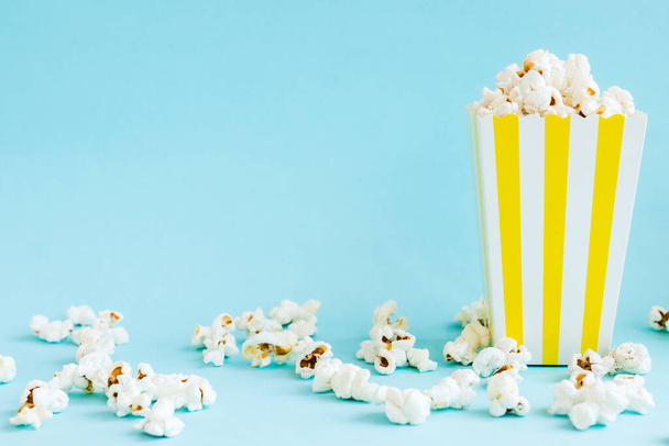 Gelb-weiß gestreifte Boxen mit Popcorn auf blauem Hintergrund. Unterhaltungskonzept. Filmabend mit Popcorn. Kinothema. - Foto, Bild