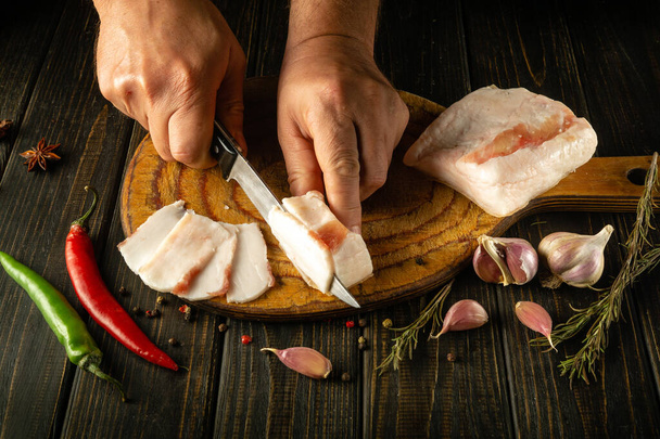 Las manos del chef cortan manteca de cerdo o salo en una tabla de cocina antes de preparar un delicioso aperitivo con ajo. Concepto de comida campesina. Vista superior. - Foto, Imagen
