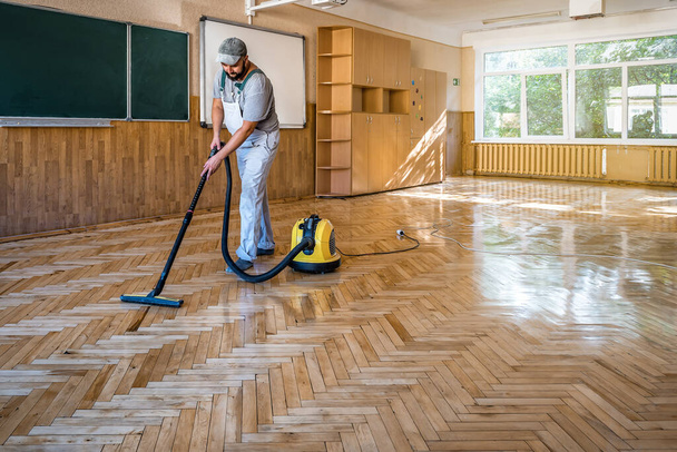 El carpintero trabajador limpia el suelo de parquet lacado con aspiradora profesional. Tema industrial - Foto, imagen