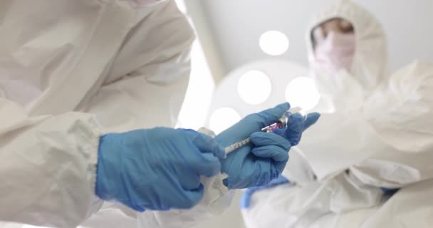Orvos védőruhában gyógyszert rajzol üvegpalackból fecskendőbe közelkép 4k film lassított felvétel. Koronavírus-fertőzés elleni védőoltás - Felvétel, videó