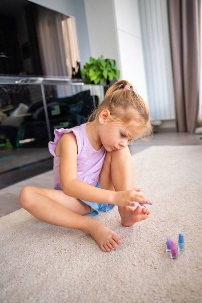 Niña haciendo pedicura y pintando uñas con esmalte de uñas de color rosa, azul y púrpura en la sala de estar en casa. Foto de alta calidad - Foto, imagen