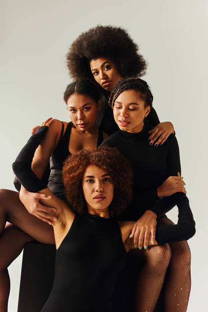 attractive african american women in black alluring outfits posing on black cube, fashion concept - Photo, Image