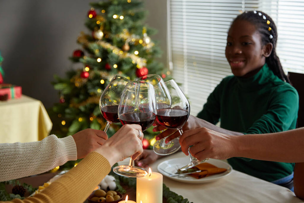 Ομάδα χαρούμενων φίλων που κάνουν πρόποση με ποτήρια κρασιού πάνω από το Χριστουγεννιάτικο τραπέζι - Φωτογραφία, εικόνα