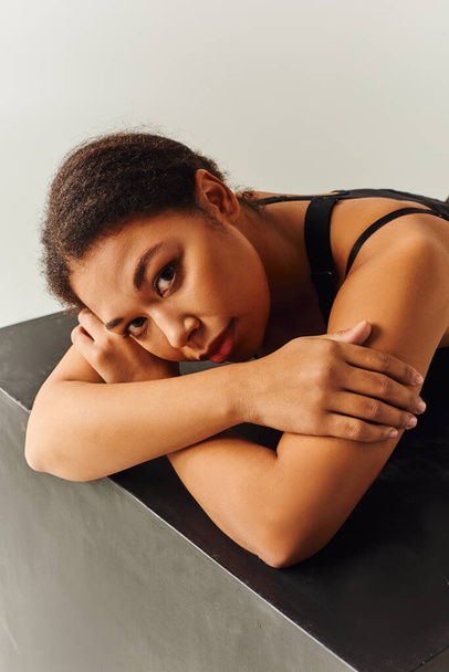 séduisant modèle féminin afro-américain en tenue sexy couché sur cube noir, concept de mode - Photo, image
