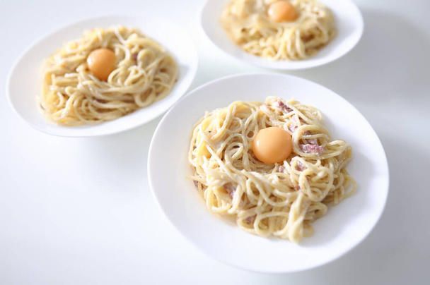 テーブルの上には3枚のスパゲッティ・カルボナーラと卵黄が添えられている。伝統的なイタリア料理のコンセプト - 写真・画像
