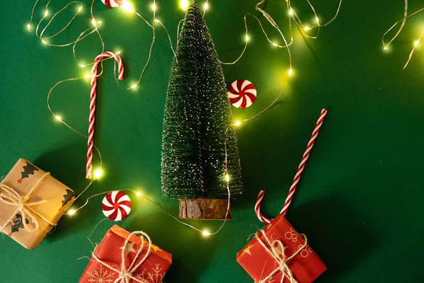 Árbol de Navidad sobre un fondo verde con luces de Navidad alrededor con dulces y regalos - Foto, Imagen
