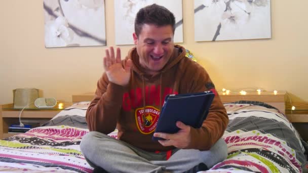 Mann macht Videokonferenz mit Tablet auf dem Bett in ihrem Schlafzimmer sitzend. 4k. - Filmmaterial, Video