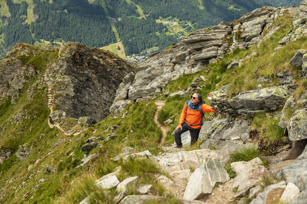 Mies pysähtyi kiipeämään kivikkoiselle polulle ja lepäsi kallioisella harjanteella, Itävallassa. Laadukas kuva - Valokuva, kuva