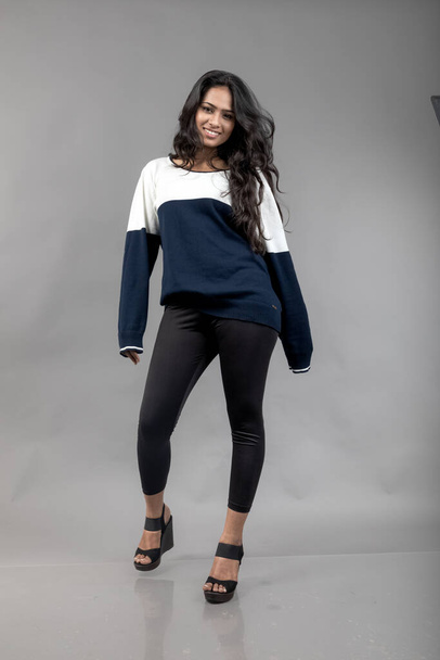 インドの若い女性モデルは,灰色の背景に対してカジュアルなウィンターウェアです. 黒いレギンス,青と白のスウェットシャツを着用したロングブラックハイレッドモデル. - 写真・画像